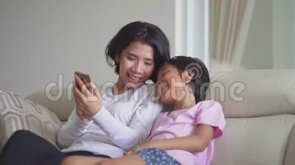 女孩和她妈妈在沙发上用智能手机视频的预览图