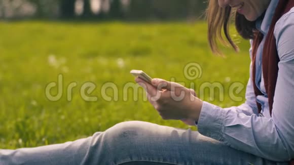 坐在草坪上的智能手机上的妇女打字文本视频的预览图