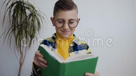 一个戴眼镜的可爱的小男孩他在家中坐在靠近白墙的地板上看书视频的预览图