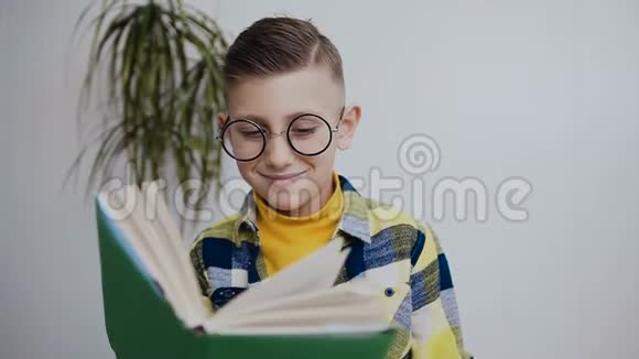 一个戴着蓝眼睛眼镜的时髦小小学生在家做作业读一本有趣的书小学生读视频的预览图