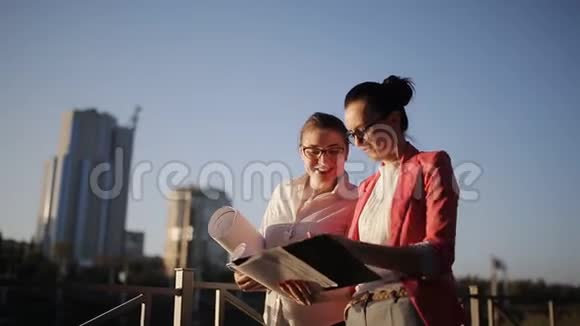 两名妇女在摩天大楼背景下的海滨绘制图纸和技术文件视频的预览图