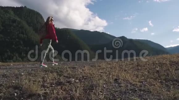 一个游客背着背包在山上的肖像戴墨镜的女旅行者爬上小山视频的预览图