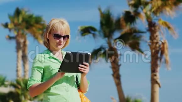 一个穿着浅绿色衬衫的女人用平板电脑对抗天空和棕榈树视频的预览图