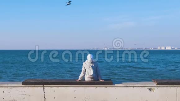 老妇人坐在沙滩上的长凳上望着大海海上的秋天后景视频的预览图