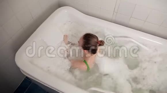 一个穿着泳衣的年轻女孩在水疗中心泡了一段时间躺在浴室里做水疗和泡沫按摩治疗美容视频的预览图