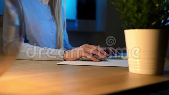 晚上在电脑上工作的女性睡在舒适的家居服里坐在木桌旁的女人的手的侧视视频的预览图
