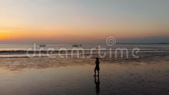 空中拍摄日落时一位年轻女子沿着海滨散步的剪影视频的预览图