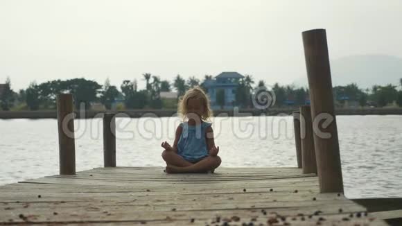 小女孩坐在木墩上摆出莲花的姿势慢慢地沉思视频的预览图