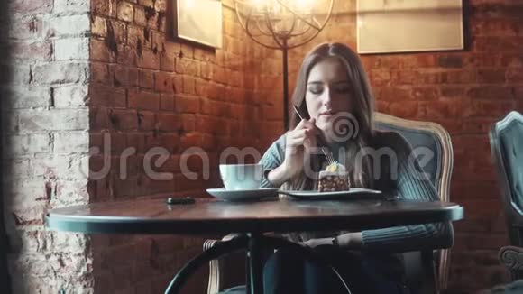 漂亮的女孩坐在咖啡馆或咖啡馆的桌子旁吃蛋糕视频的预览图