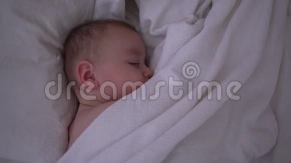 一个正在睡觉的可爱的幼儿慢慢地躺在白色毯子下面视频的预览图