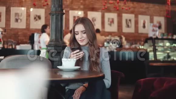 咖啡馆里一个迷人女孩的肖像一个女孩在咖啡屋的一张桌子旁的智能手机上重写视频的预览图