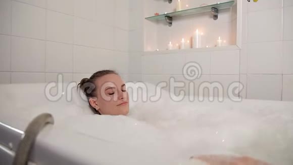一个穿着泳衣的年轻女孩在水疗中心泡了一段时间躺在浴室里做水疗和泡沫按摩治疗美容视频的预览图