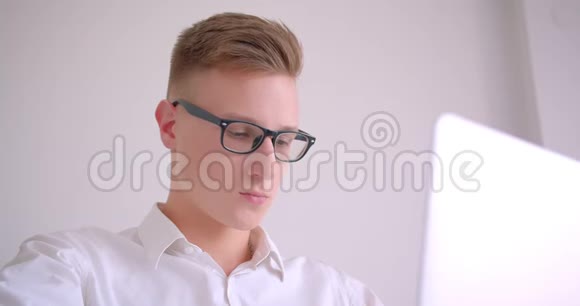 年轻英俊的白种人商人戴着眼镜用手提电脑看着相机开心地笑着的特写照片视频的预览图