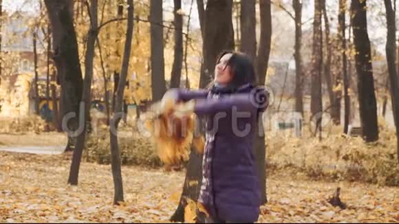 快乐的年轻漂亮的黑发女人在公园里扔秋叶视频的预览图