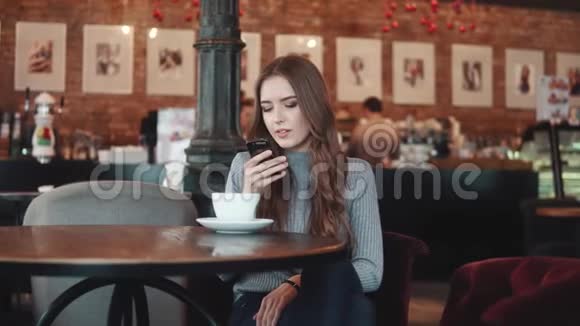 一个漂亮的女孩坐在咖啡馆里用手机发短信视频的预览图