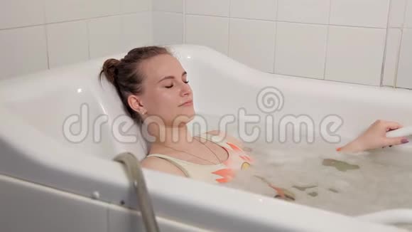 一个穿着泳衣的年轻女孩在水疗中心度过了一段时间她躺在浴室里用水疗按摩视频的预览图