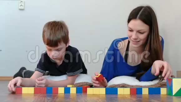 妈妈和儿子一起玩的木制彩色教育玩具积木躺在地上把立方体铺成一条线视频的预览图