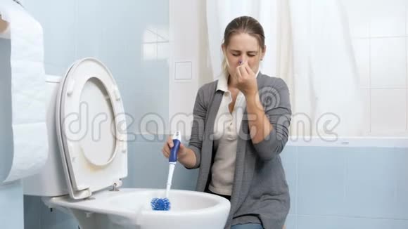 4k镜头显示一位尖叫的年轻女子在家洗脏厕所时鼻子紧闭视频的预览图