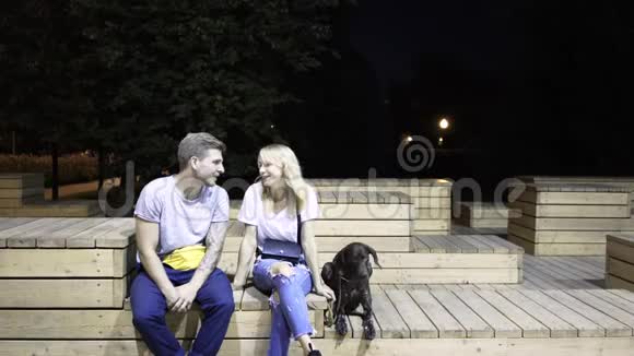 年轻夫妇拥抱亲吻他们的狗在他们附近夜间公园视频的预览图