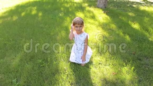 一个可爱的小女孩坐在公园的草地上视频的预览图