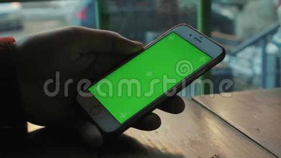一个男人在木桌旁的咖啡馆用绿色屏幕的手机视频的预览图