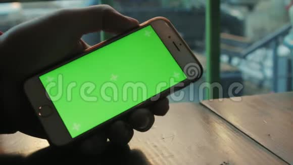 一个男人在木桌旁的咖啡馆用绿色屏幕的手机视频的预览图