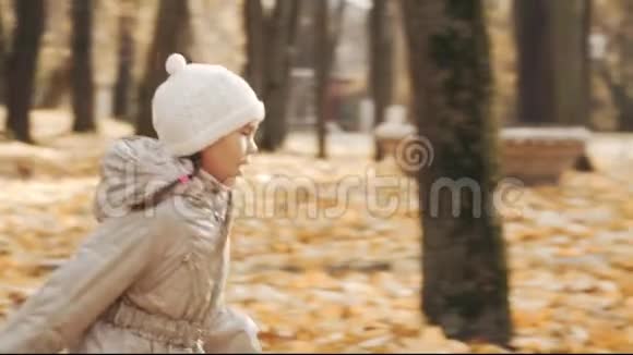 快乐的小女孩带着秋天的树叶在公园里奔跑视频的预览图