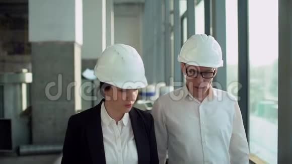 男女执行工程师戴着安全帽在工厂车间里走来走去讨论这件事慢动作视频的预览图