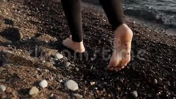 苗条的年轻女子赤足的双腿正迈过靠近海水的卵石滩视频的预览图