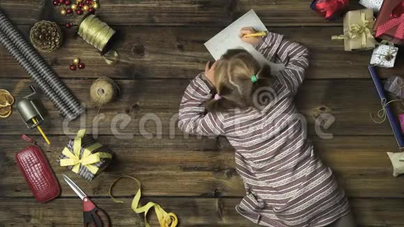 头顶上的女孩用手工艺品工具在老式木桌上写圣诞老人的礼物信垂直顶部视图视频的预览图