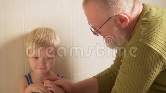 快乐的老人从他的手和脸到他的小儿子用毛巾擦拭他的手父亲照顾视频的预览图