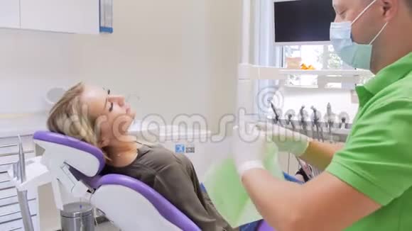 男性牙医在牙齿治疗前将保护组织贴在病人身上的4k镜头视频的预览图