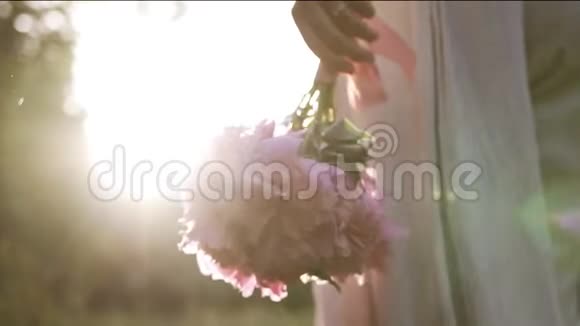 美丽的低角度视角一个苗条的女人走在户外手里拿着粉红色的牡丹花太阳照耀着视频的预览图