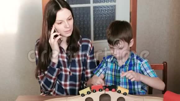 一起玩妈妈在打电话儿子正在玩一条铁路坐在火车马车和隧道旁视频的预览图