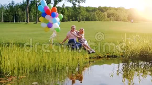 快乐的年轻人拥抱坐在河岸上的女孩的慢镜头视频的预览图