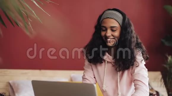 漂亮的女孩穿着粉红色睡衣家里坐在床上用笔记本电脑年轻女子微笑着聊天视频的预览图