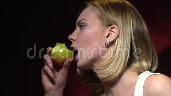 一个金发女人在深红色背景下吃一个绿色苹果的慢镜头拍摄视频的预览图