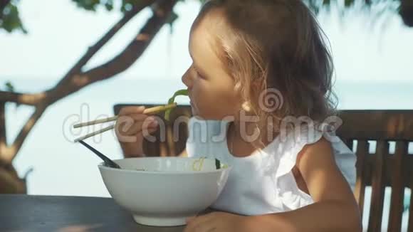 女孩在露天海滩咖啡馆用筷子吃面条汤视频的预览图