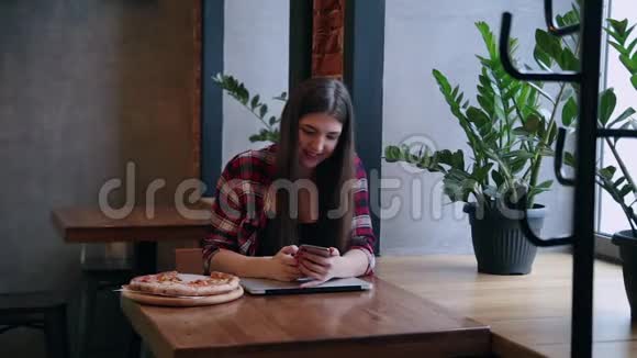 漂亮迷人的商务女性坐在咖啡馆的桌子上拿着手机和笔记本电脑桌子上有披萨视频的预览图