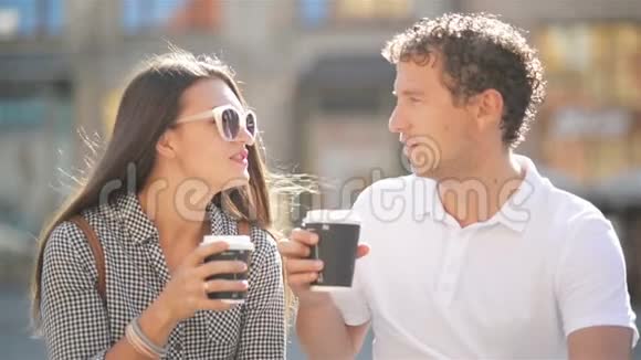 阳光明媚的夏日可爱的情侣坐在城市广场的长凳上喝咖啡的特写镜头视频的预览图