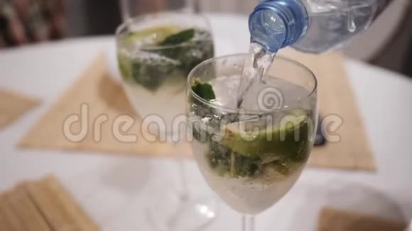 莫吉托鸡尾酒的制作起泡的水被倒入一个带有薄荷和石灰的玻璃杯中视频的预览图