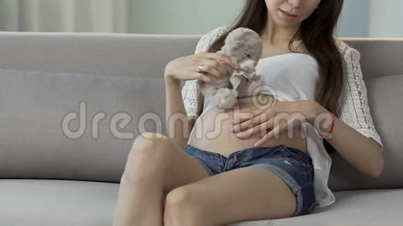 怀着孩子的女人抱着玩具熊在肚子附近玩耍期待视频的预览图