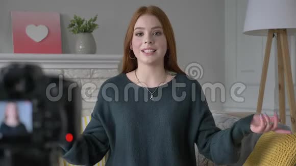 年轻的红发女孩博客写手微笑着对着镜头说话使自己成为一个发型衣服家里的舒适视频的预览图