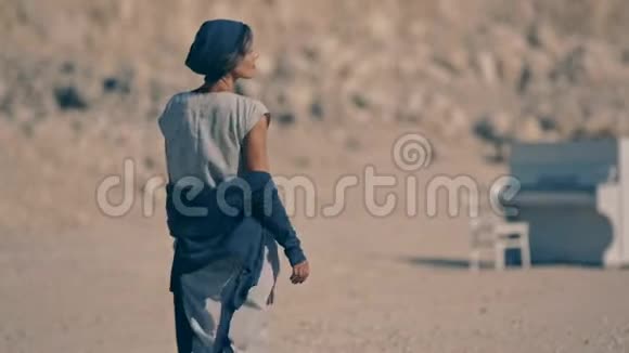 疲惫的年轻女子光着脚走在山峦和白色钢琴背景的砾石上视频的预览图