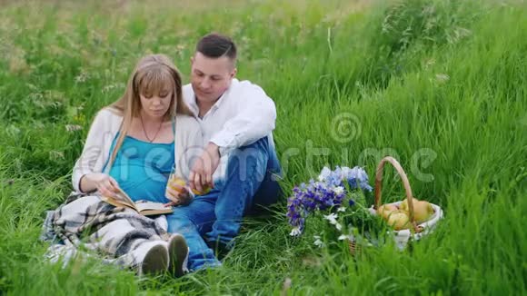 未来的父母在公园里放松看书坐在绿草上视频的预览图