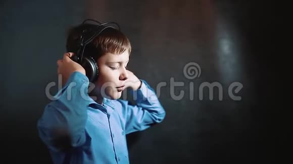耳机小男孩在黑色背景下听音乐工作室年轻的金发欧洲德国男孩戴着耳机摇着视频的预览图