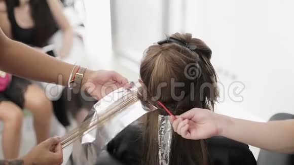 一个有纹身男人用铝箔和刷子在长长的女性头发上涂上油漆视频的预览图