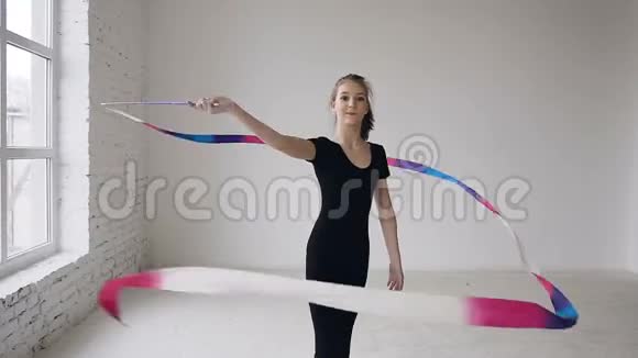 带彩色磁带的灵活体操运动员在室内以白色背景创造出优美优美的动作视频的预览图