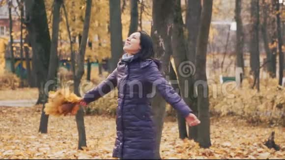 快乐的年轻漂亮的黑发女人在公园里和秋天的树叶旋转视频的预览图