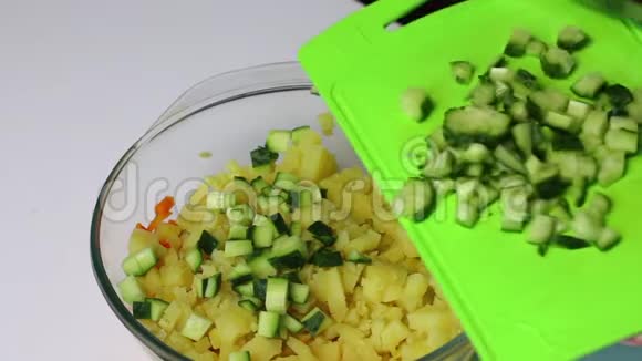 俄罗斯肉类沙拉配蔬菜和蛋黄酱一个女人正在砧板上切黄瓜然后将其添加到容器中视频的预览图